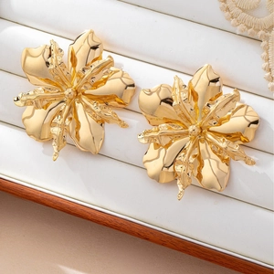 Detailed macro view of large gold metallic flower earrings with irregular textured petals