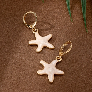 Golden starfish dangle earrings with cream enamel finish on a sandy beach background
