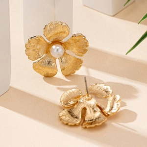 Boucles d'oreilles fleurs dorées élégantes avec texture brossée et perle sur fond neutre