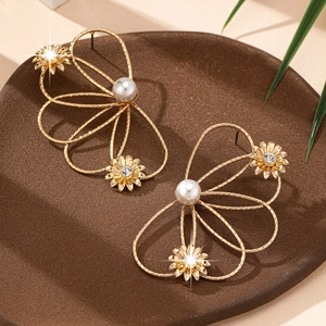 Elegante goldene hohle Blumenohrringe mit weißen Perlen auf einem Keramiktablett