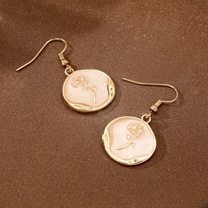 Boucles d'oreilles pendantes dorées avec fleurs en émail sur un fond en tissu texturé
