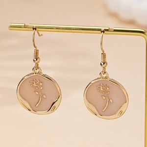 Élégantes boucles d'oreilles rose en émail doré présentées sur un support en métal