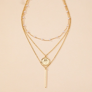 Détail d'un collier doré triple couche avec perles, pièce rose et pendentif barre