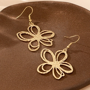 Elegant gold butterfly drop earrings with hammered metal texture on a rustic ceramic plate