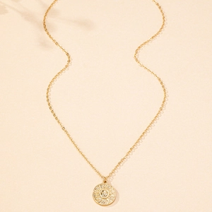 Close-up of vintage gold sun face pendant necklace on minimalist textured beige surface