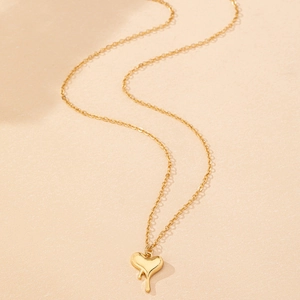 Detailed view of a gold dripping heart pendant necklace on a minimalist beige background