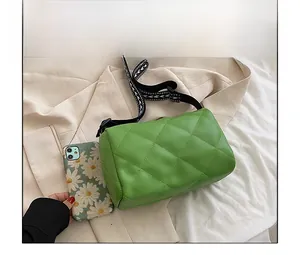 Cylindrical green quilted bag with geometric strap compared to a smartphone