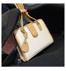 Detail of a white pleated tote bag with brown leather handles in a car interior setting