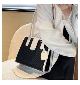 Detail of contrast color tote bag with black pleated texture and cream leather handles