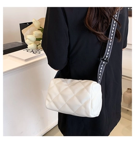 Detailed view of white quilted cylinder bag with geometric patterned strap on model