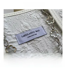 Détail du tissu plissé blanc avec chaîne florale argentée et étiquette de marque tissée