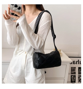 Detail of black quilted cylindrical crossbody bag with wide geometric pattern strap