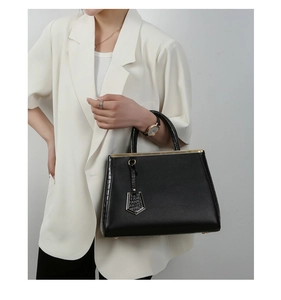 Dettaglio borsa nera con trama a coccodrillo indossata da modella in completo beige