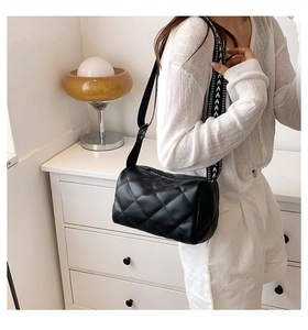 Detail of black quilted cylindrical crossbody bag with wide geometric pattern strap