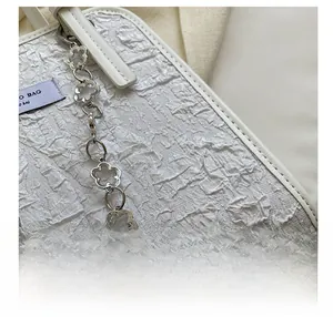 Détail du sac cabas blanc avec texture froissée et bandoulière chaîne à fleurs argentées