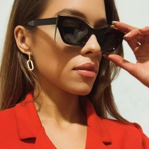 Close-up of black cat-eye sunglasses and gold chain earrings on a woman in red