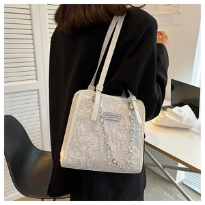 Détail du sac cabas blanc avec texture froncée, chaîne argentée et étiquette de marque