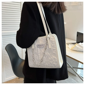 Détail d'un sac à main blanc texturé avec chaîne argentée porté sur un blazer noir