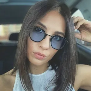 Retro cat-eye sunglasses with black metal frames and light blue lenses worn inside a car