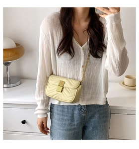 Close-up of beige quilted chain bag with V-shaped stitching and golden metal lock detail