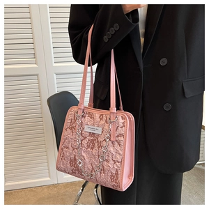 Détail d'un sac cabas rose texturé avec chaîne argentée et étiquette logo en cuir