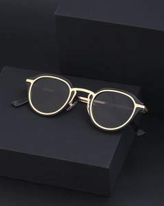 Detailed close-up of retro cat-eye sunglasses with black and gold metallic frame on black stand