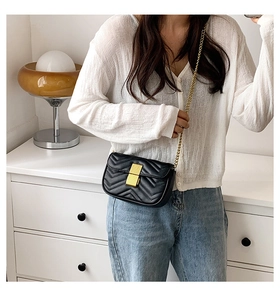 Detail view of black quilted crossbody bag with gold chain strap and metal clasp closure