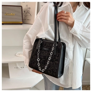 Détail d'un sac cabas noir gaufré avec chaîne à fleurs argentée sur un mannequin