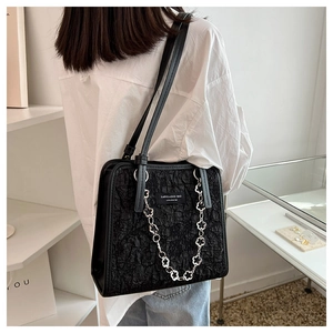 Détail du sac cabas plissé noir avec chaîne florale argentée et logo sur l'épaule