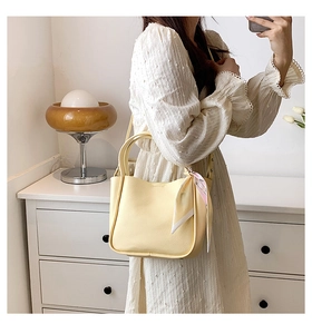 Detail of pale yellow bucket bag with lychee texture and floral scarf on handle