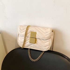 Elegant beige V-quilted crossbody bag with gold chain strap on a black chair