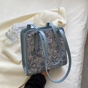 Sac fourre-tout plissé bleu et gris avec chaîne florale sur fond de blazer beige
