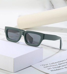 Detail view of dark green square sunglasses with thick frames and grey lenses on marble