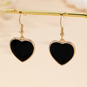Détail de boucles d'oreilles cœur en or et émail noir sur un présentoir doré