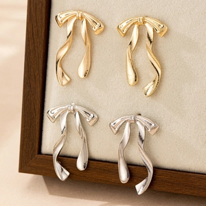 Elegant gold and silver bow ribbon tassel earrings displayed on a beige jewelry stand