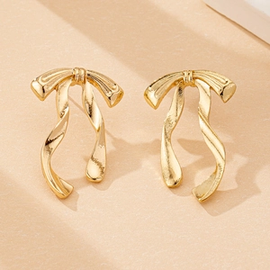 Close-up of elegant gold ribbon bow earrings on a textured warm beige surface