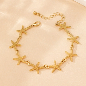 Detail shot of a golden starfish link bracelet with adjustable lobster clasp on sand texture
