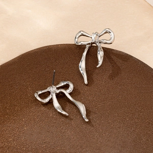 Elegant silver metallic bow earrings on a display stand with soft natural lighting