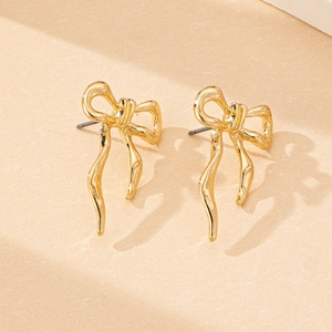 Macro detail of golden bow earrings featuring elegant irregular textured metal finish