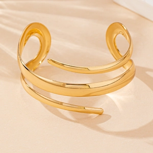 Detail of a gold-plated spiral open bangle with high-polished teardrop curved lines