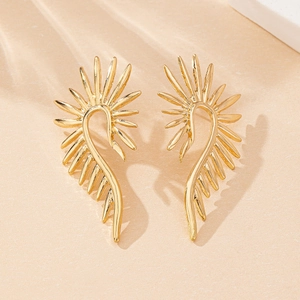 Close-up of golden sunburst stud earrings with polished feather textures on a beige surface