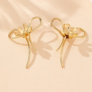 Detailed close-up of polished gold flower bow earrings on beige textured surface