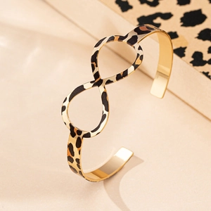 Golden infinity symbol cuff bracelet with leopard print pattern on beige background