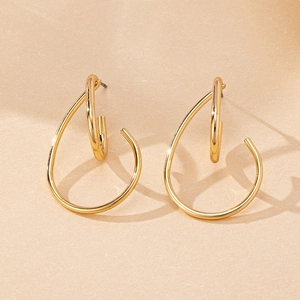 Detailed view of gold-plated geometric double-loop teardrop earrings on textured beige