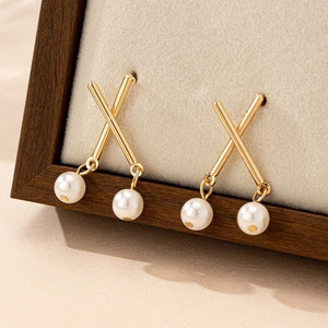 Elegant X-shaped gold earrings with white pearls displayed on a beige jewelry stand