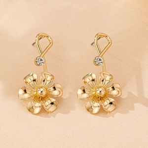 Détail de boucles d'oreilles fleurs dorées avec texture soie et clou à strass noué