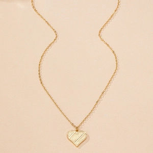Détail d'un pendentif coeur doré avec texture sablée et lignes diagonales élégantes