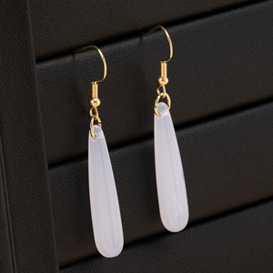 Boucles d'oreilles pendantes dorées avec pierres en résine blanc crème sur boîte à bijoux