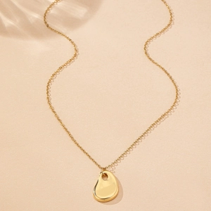 Macro shot of polished gold water drop pendant necklace with wavy light reflections