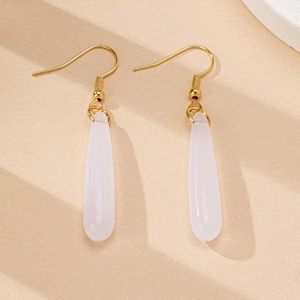 Détail de boucles d'oreilles dorées avec pendentifs en résine rose sur fond beige